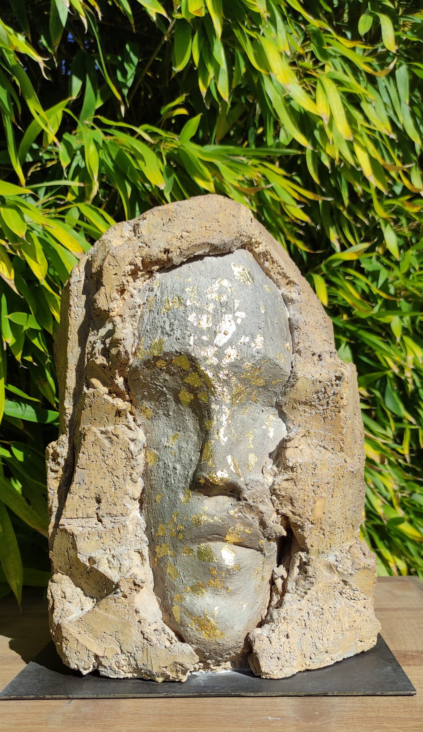 Sculpture en terre cuite patinée avec feuille d'or. Visage sortant de la roche